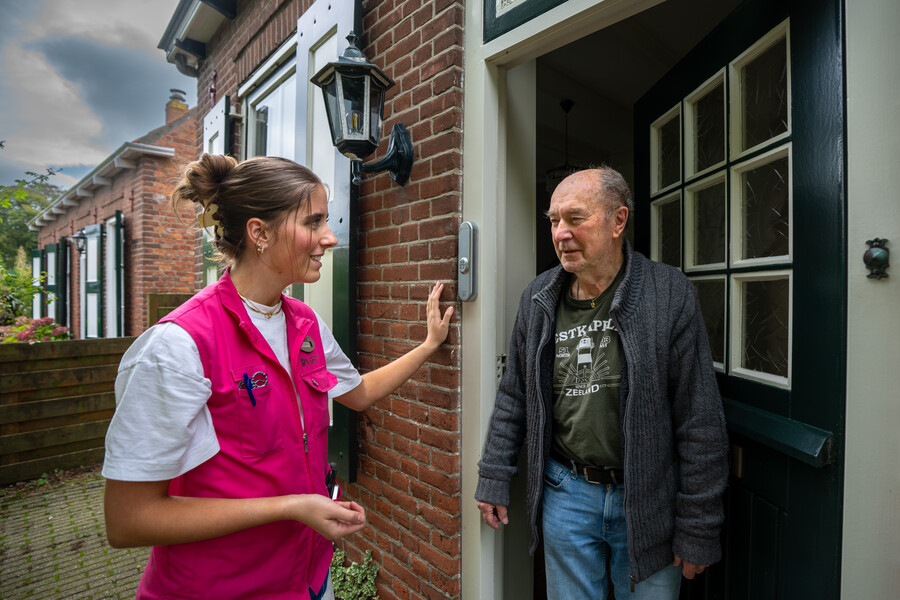 Een medewerker ZorgThuis in gesprek aan de voordeur bij een cliënt