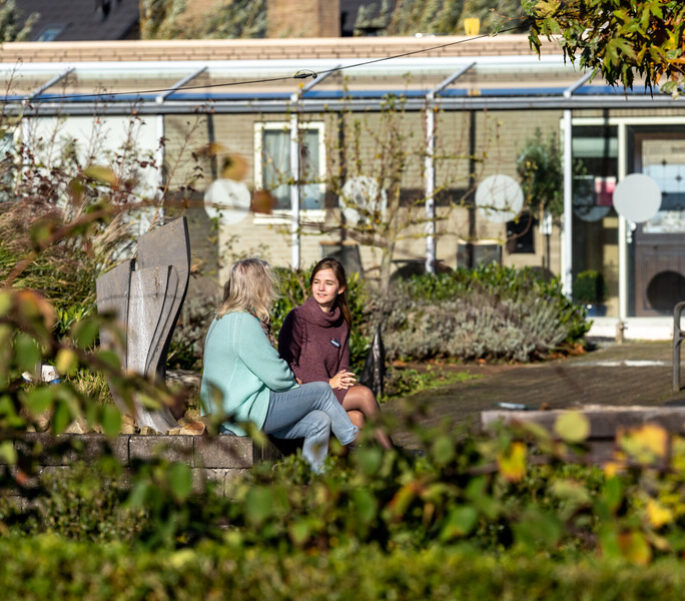 Een medewerker zit buiten en is in gesprek met een cliënt