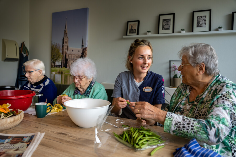 Cliënten doppen de boontjes en schillen de aardappelen met hulp van een medewerker