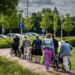 Een groep vrijwilligers wandelt met cliënten in een rolstoel