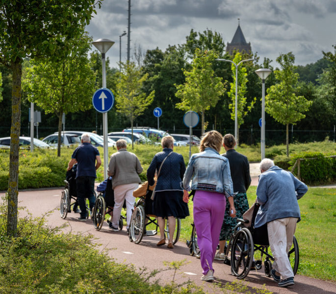 Een groep vrijwilligers wandelt met bewoners in een rolstoel