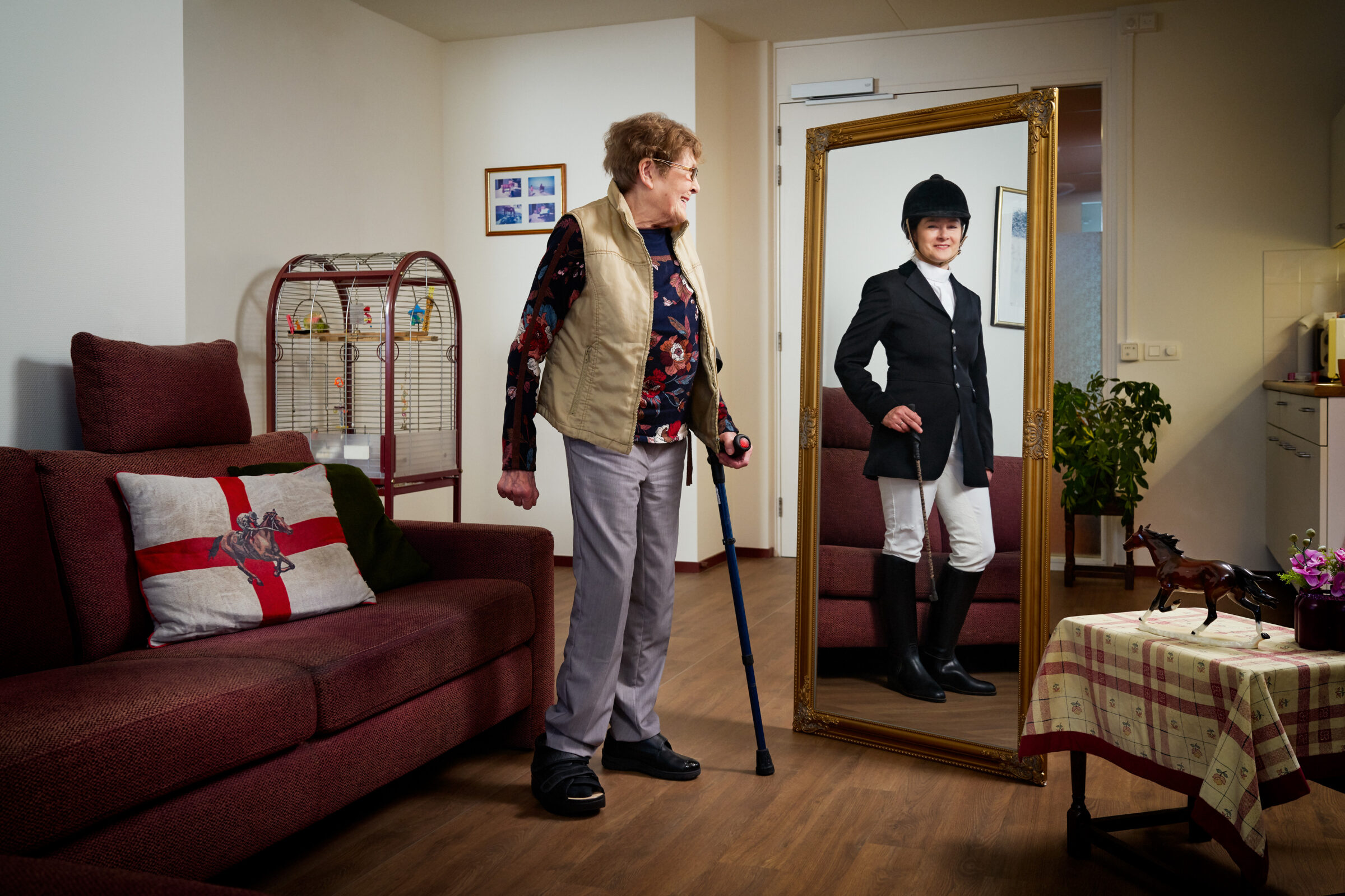 Mevrouw kijkt in de spiegel naar een jongere versie van haarzelf in paardrij kleding.