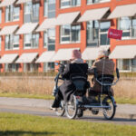 Een medewerker en een cliënt fietsen buiten op straat in een duofiet