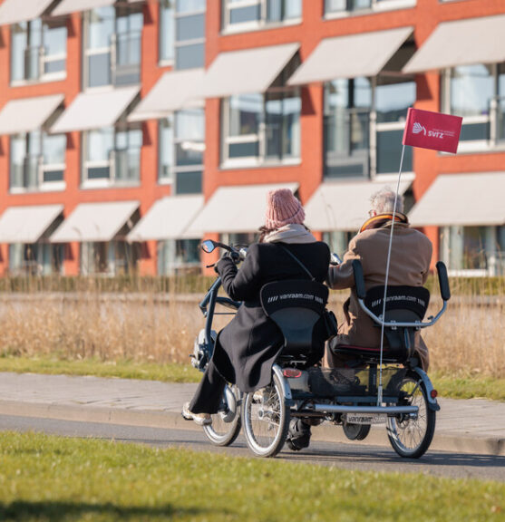 Een medewerker en een cliënt fietsen buiten op straat in een duofiet
