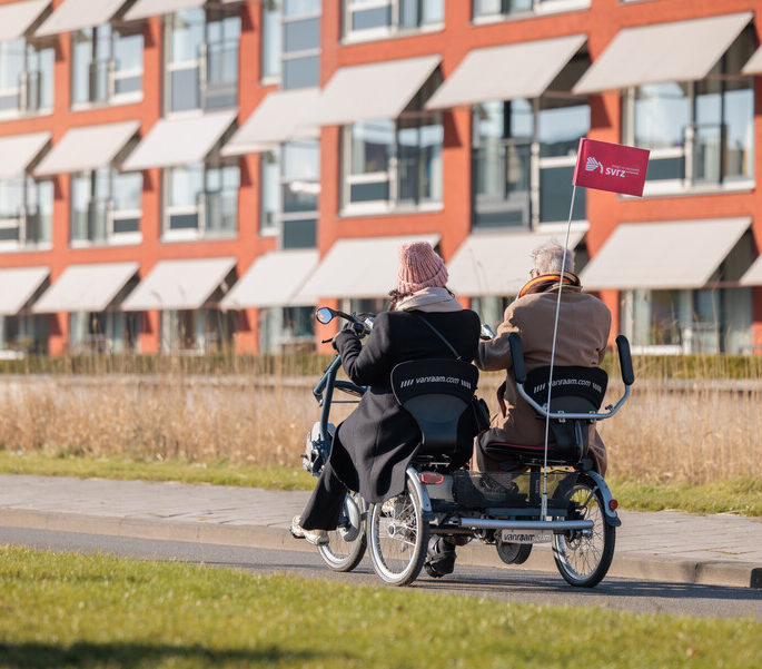 Een medewerker en een cliënt fietsen buiten op straat in een duofiet