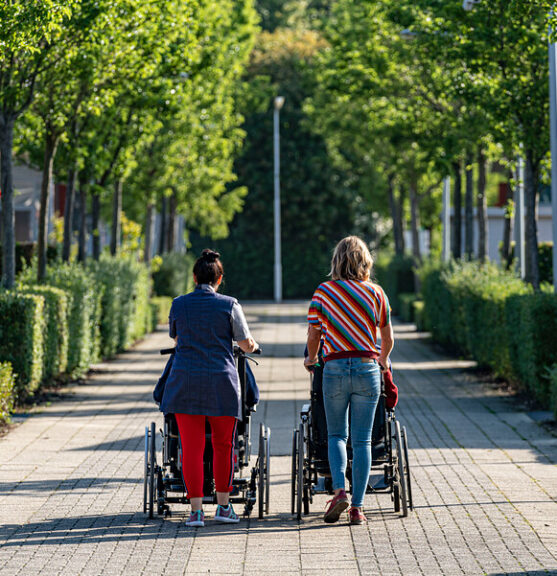 Twee vrouwen wandelen met cliënten in een rolstoel