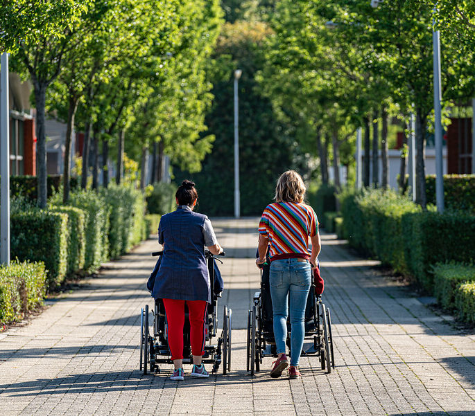 Twee vrouwen wandelen met cliënten in een rolstoel
