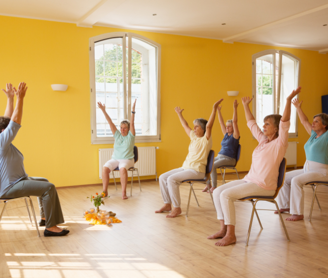Een groep ouderen doet onder begeleiding op een stoel yoga oefeningen