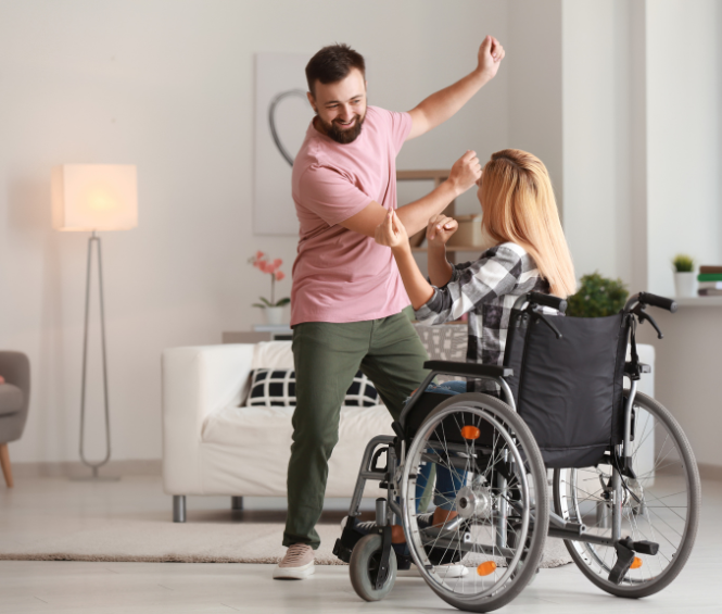Een vrolijke man danst samen met een vrouw in een rolstoel