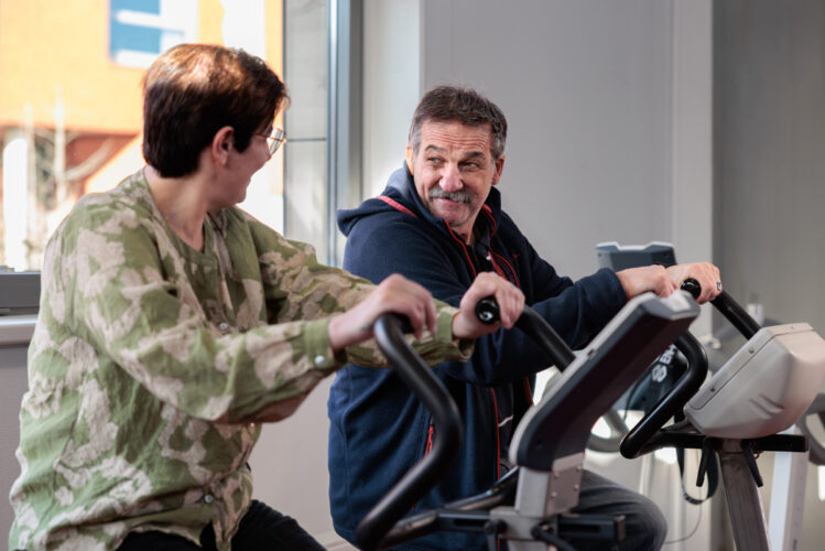 Medewerker en cliënten fietsen naast elkaar op een hometrainer