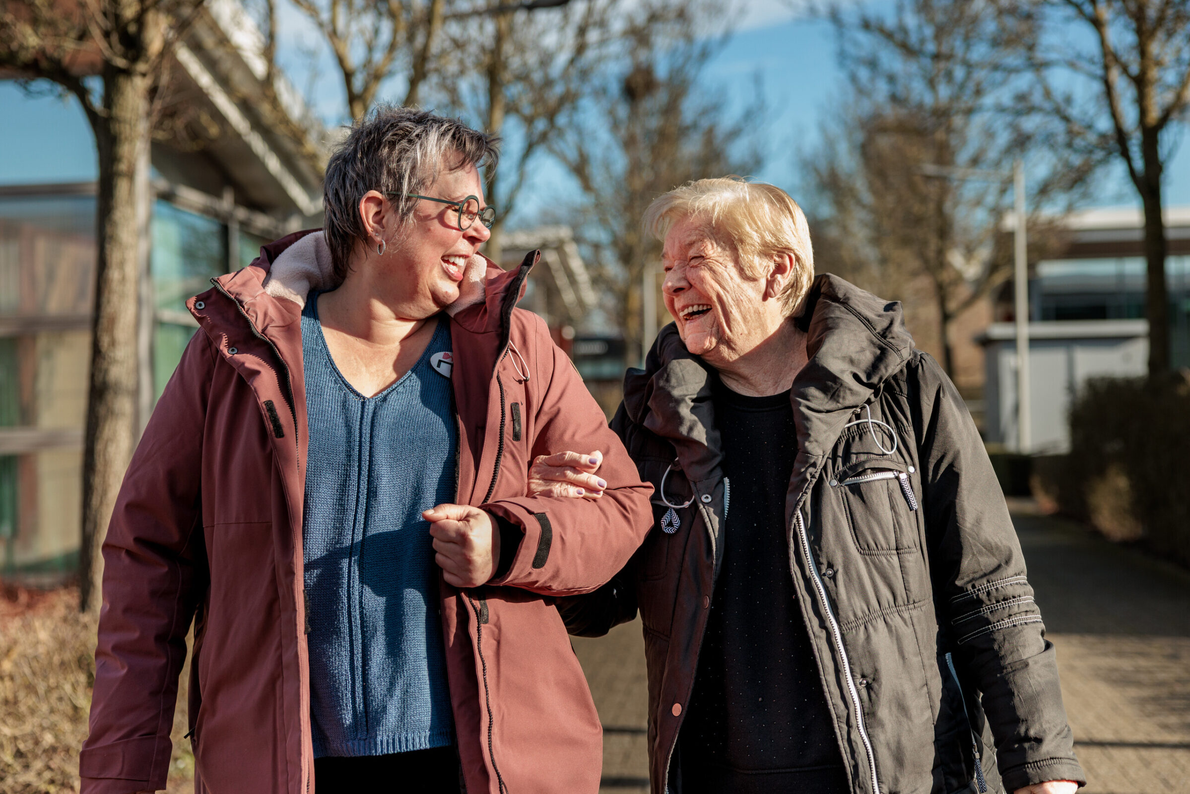 Bewoner en medewerker wandelen arm in arm in de tuin
